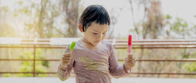 The happy kid girl in a wet shirt eating ice cream popsicle in the natural outdoor background