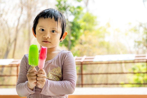 The happy kid girl in a wet shirt eating ice cream popsicle in the natural outdoor background.