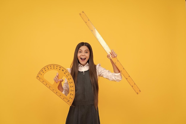 Happy kid hold math protractor and ruler in school on yellow background education