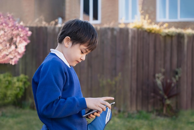 Happy kid holding tablet pc standing outside waiting for School bus Child boy playing game online or reading story on internet Preschool boy learning with modern technologyBack to school concept