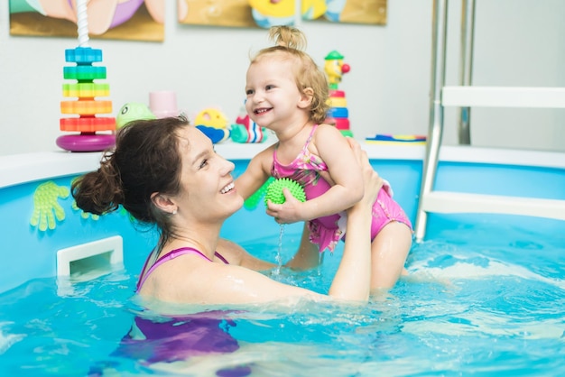 Happy kid learning to swim with mom in the pool