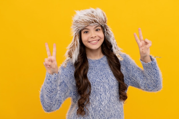 Happy kid long hair in hat show peace gesture on yellow background, fashion