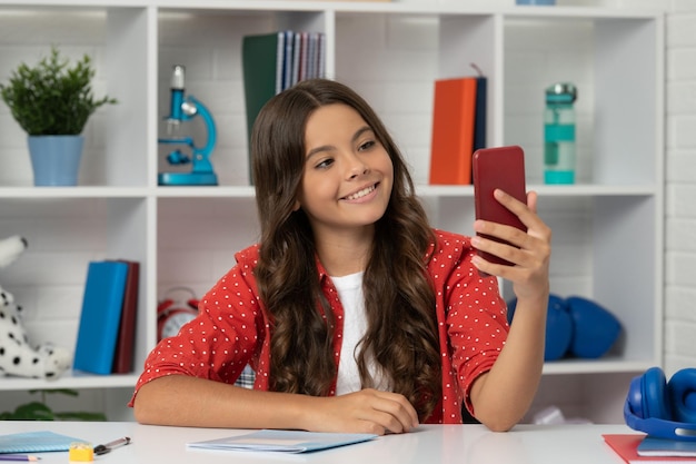 Happy kid making selfie in classroom september 1 child making video blog blogging on phone vlogger with cellphone young influencer teen girl blogger use smartphone back to school