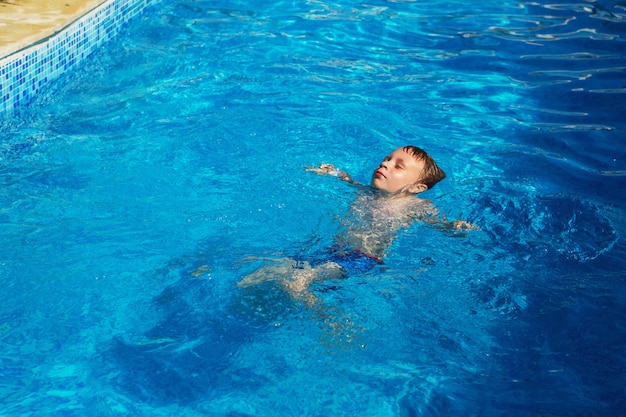 Happy kid playing in blue water of swimming pool on a tropical resort at the sea