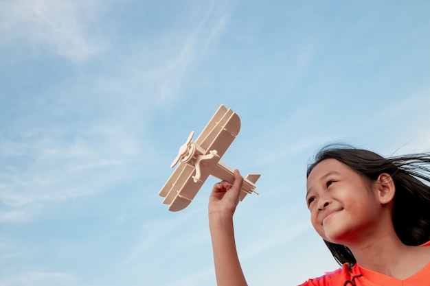 Happy kid playing with toy wooden airplane against sunset sky