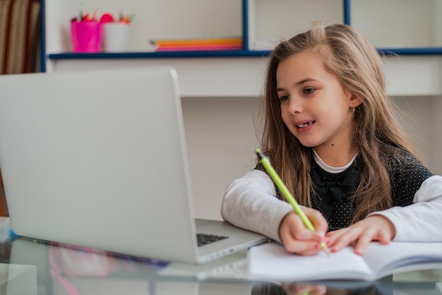 A happy kid student writing in a notebook while learning for school at the home desk