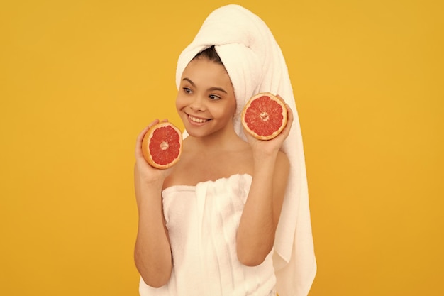 Happy kid in towel with grapefruit on yellow background