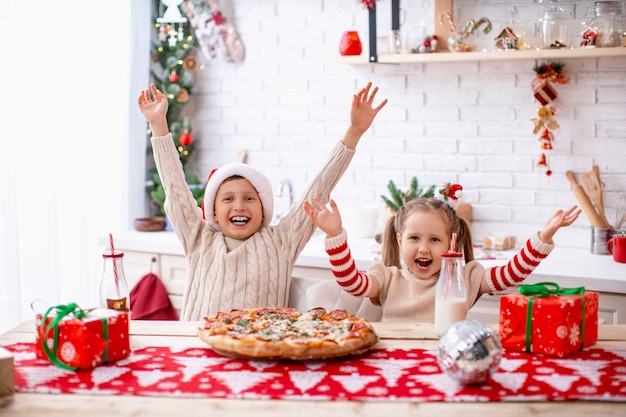 Happy kids brother and sister eating pizza in the kitchen