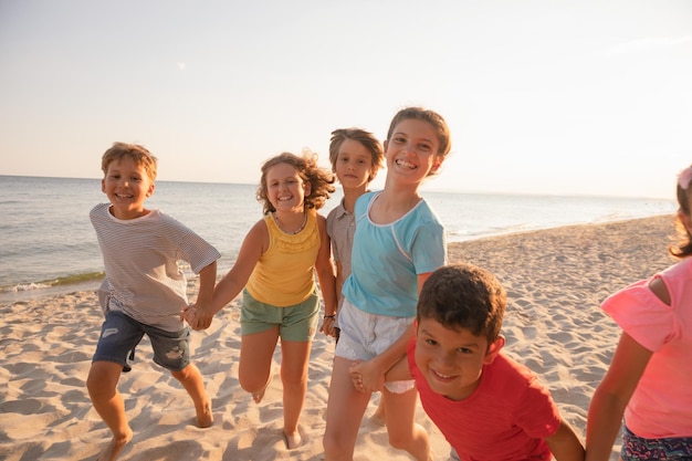 Happy kids running on the beach Cheerful children having good time at summer holidays Smiling boys and girls on vacation on seashore