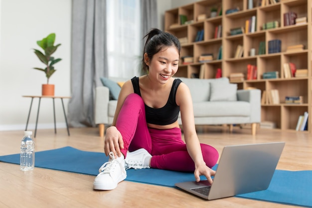 Happy korean fitness blogger looking at laptop chatting and choosing online workout lesson at home