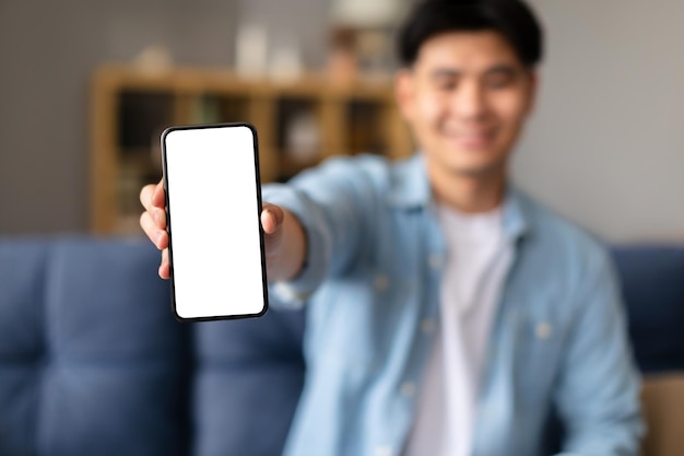 Happy korean man showing cellphone with empty screen at home