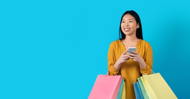 Happy korean woman with shopping bags using smartphone copy space