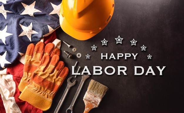 Happy Labor day concept American flag with different construction tools and the text on dark stone background