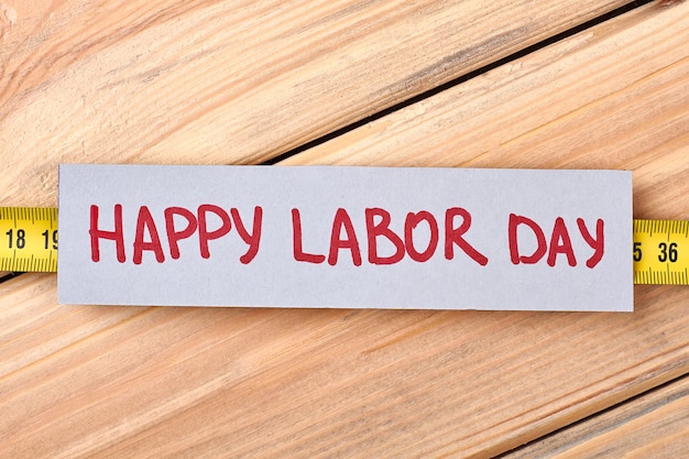 Photo happy labour day greeting paper. tape measure on wooden background. handmade congratulation card.