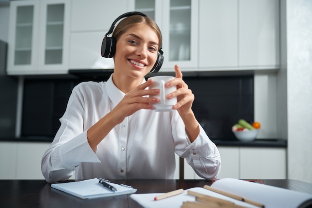 Happy lady in headphones sitting at table and drinking tea