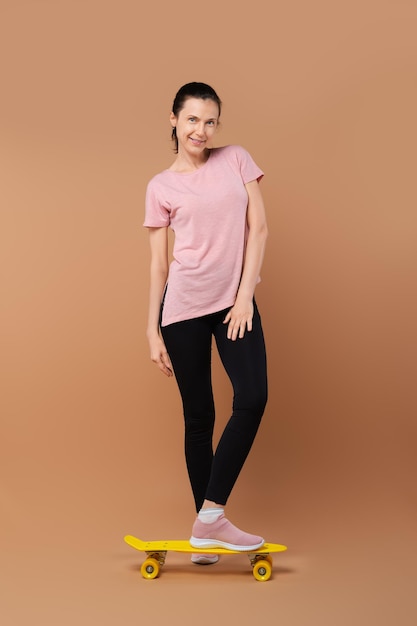 Happy lady in sportive outfit posing in studio with skateboard