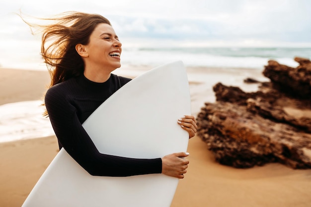 Happy lady in swimsuit holding surfboard under arm going to have surfing training on ocean sea background