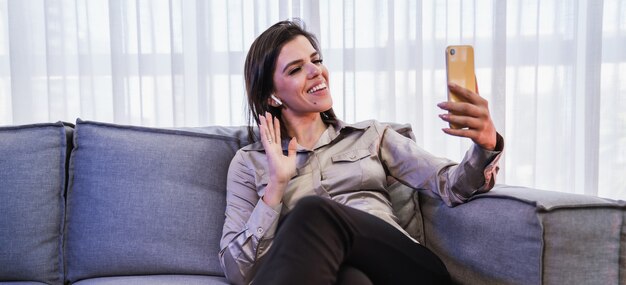 Happy Latin lady sit on room pose share good news at social media via cellphone.