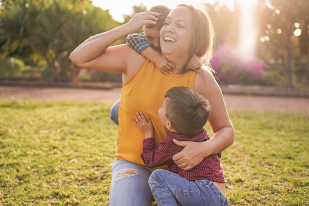 Happy latin mother having playful time with twin sons at city park - Family, mother and children love