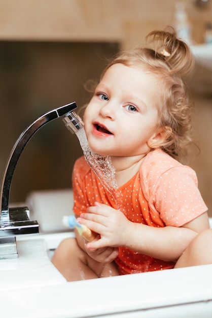 Happy laughing baby girl brushing her teeth in the bath