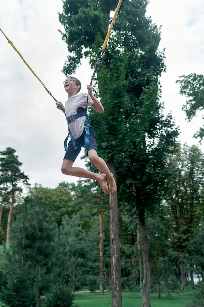 Happy laughing boy hangs on slings jumps high on trampoline in an amusement park Teenager is having fun