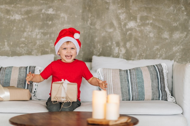 Happy laughing Caucasian boy in red Santa Claus receiving his presents on Christmas morning Child excited and smiling Opening gifts Copy space