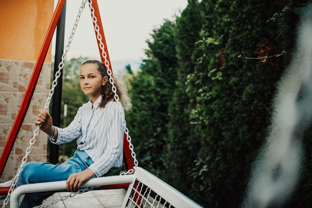 Happy laughing girl posing on swing in sunset summer