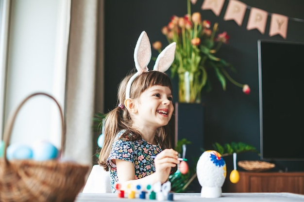 Happy laughing little girl with bunny ears painting gypsum Easter egg