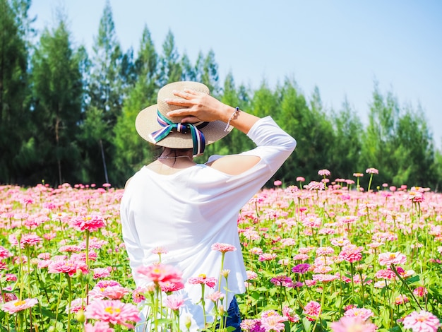 Happy life of young Thai women wear fashion straw hat traveling and relaxing in flower garden of Zinnia.