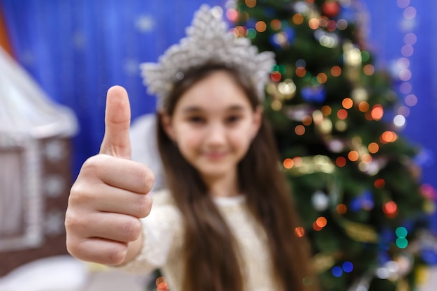 Happy little 10 years girl show thumb up sign ok looking at camera in christmas decorated home i