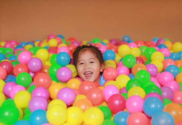 Happy little Asian child girl playing with colorful plastic balls playground.