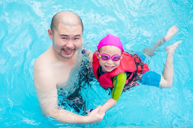 Happy little asian girl learning to swim with her father in swimming pool