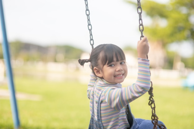 Happy little Asian girl playing swing outdoor in the park