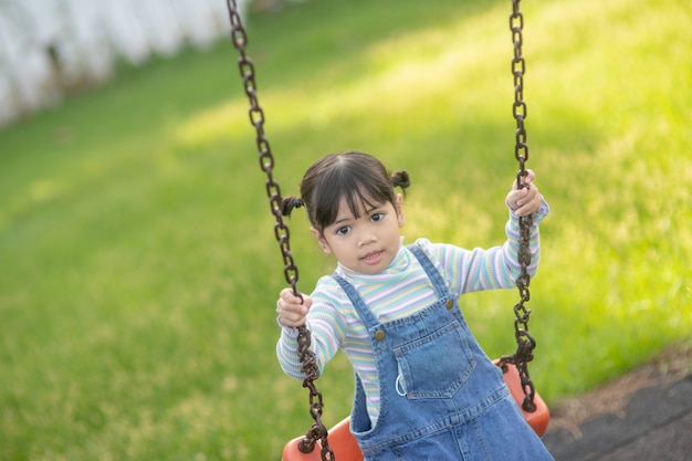 Happy little Asian girl playing swing outdoor in the park