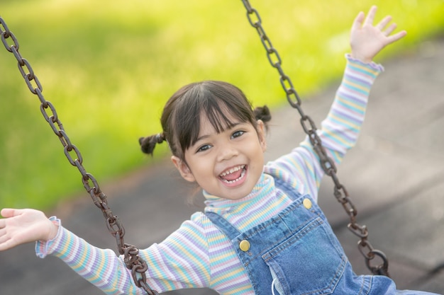 Happy little Asian girl playing swing outdoor in the park