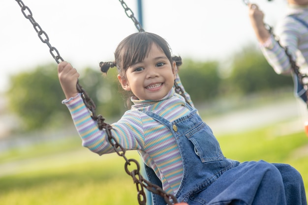 Happy little Asian girl playing swing outdoor in the park