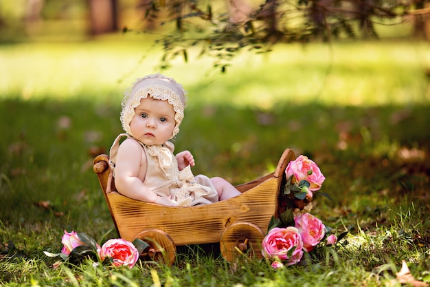 Happy little baby girl in a cart with rose flowers outdoors in summer.