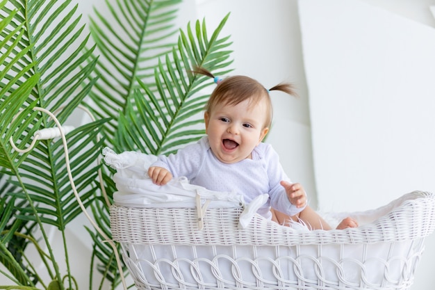 Happy little baby girl sitting in a beautiful stroller in a white bodysuit at home