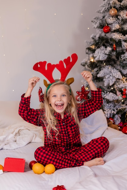 a happy little blonde girl in pajamas at Christmas looks at New Year's gifts and plays with New Year