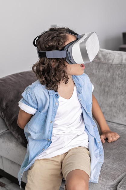 Happy little boy child using virtual reality headset vr glasses gesturing at home having fun