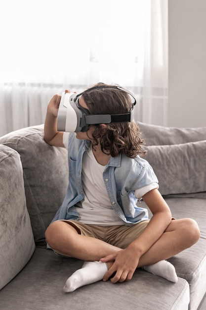 Happy little boy child using virtual reality headset vr glasses gesturing at home having fun