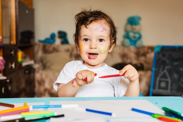 Happy little boy draws with colorful markers on a piece of paper