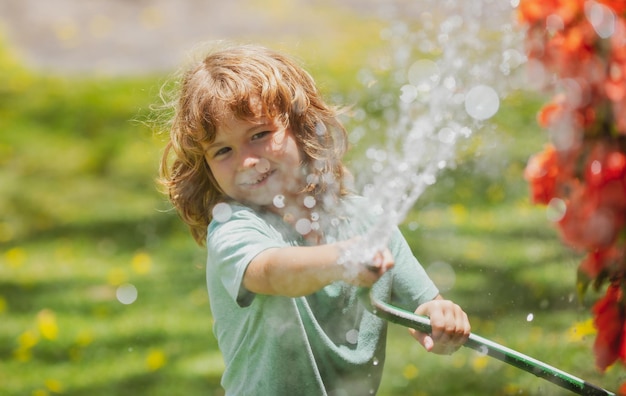 Happy little boy having fun in domestic garden child hold watering garden hose active outdoors games