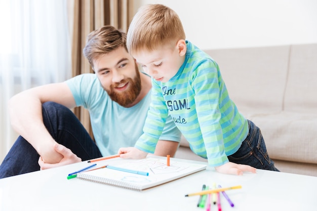 Happy little boy and his father drawing together at home