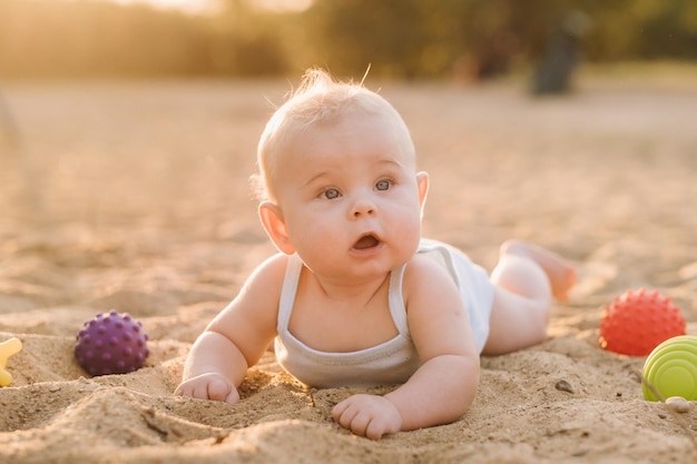 A happy little boy is lying on a sandy beach near the sea in the rays of the setting sun