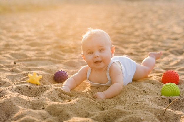 A happy little boy is lying on a sandy beach near the sea in the rays of the setting sun