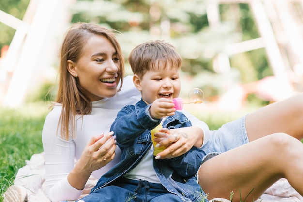 Happy little boy is playing blowing soap bubbles together with his happy young mother Weekend breaks caring parenting and child care