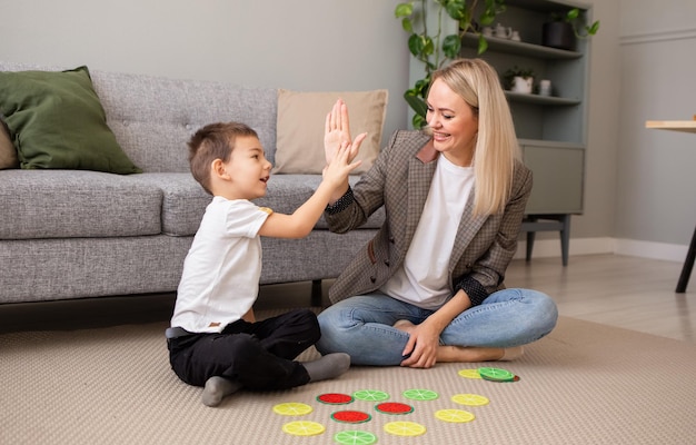 A happy little boy is playing with his mother on the carpet in the room in an educational logic game Early development of intelligence