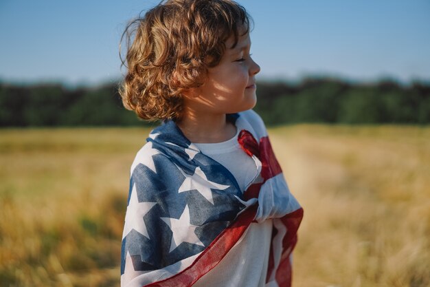 Happy little boy patriot running in the field with American flag. USA celebrate 4th of July