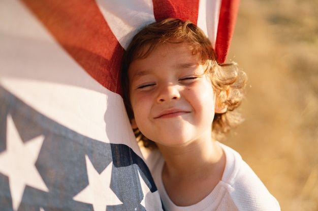 Happy little boy patriot running in the field with American flag. USA celebrate 4th of July